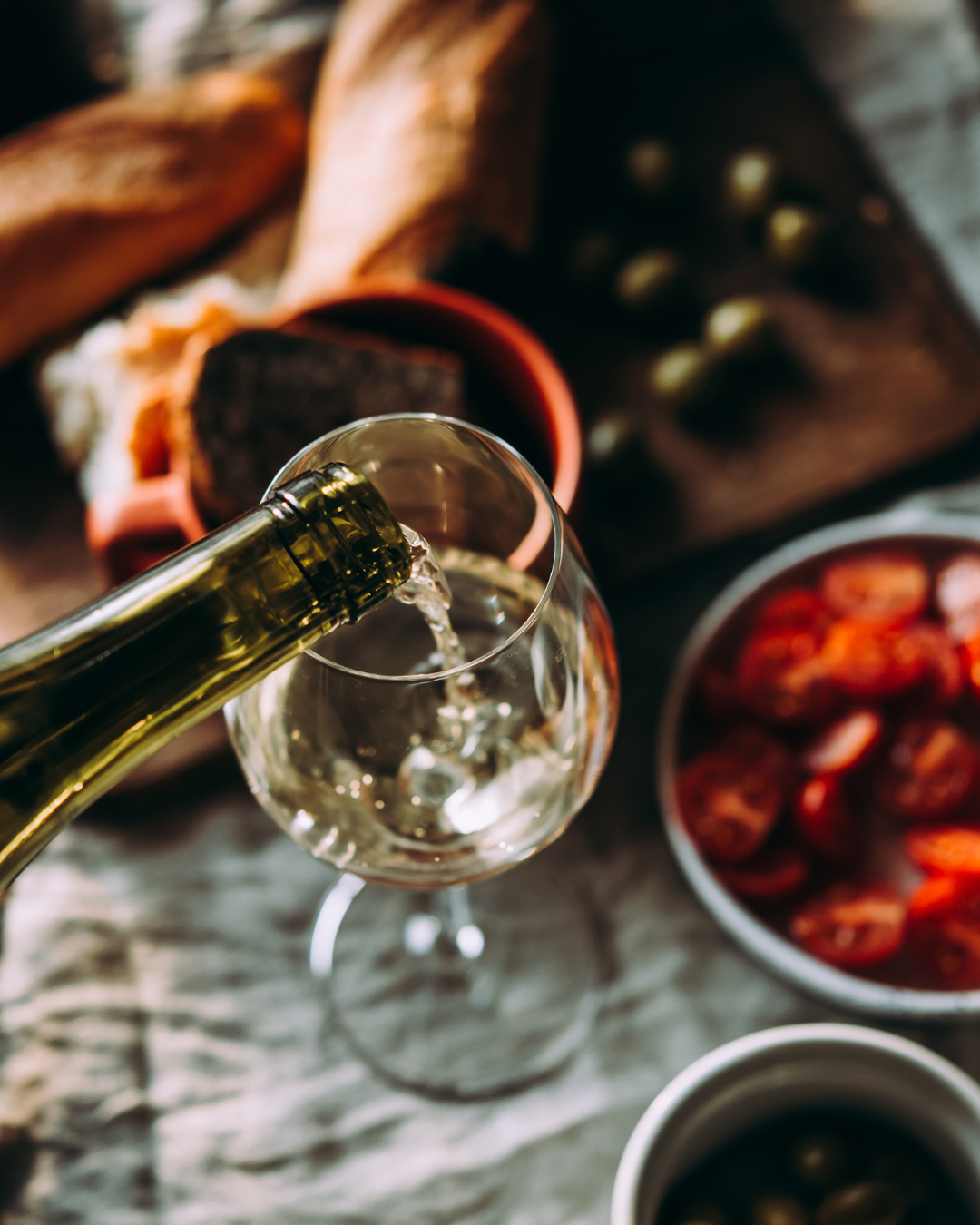 Wine being poured into a glass with a rustic setting featuring bread and dried fruits.