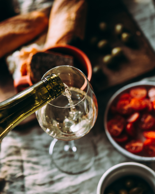 Wine being poured into a glass with a rustic setting featuring bread and dried fruits.
